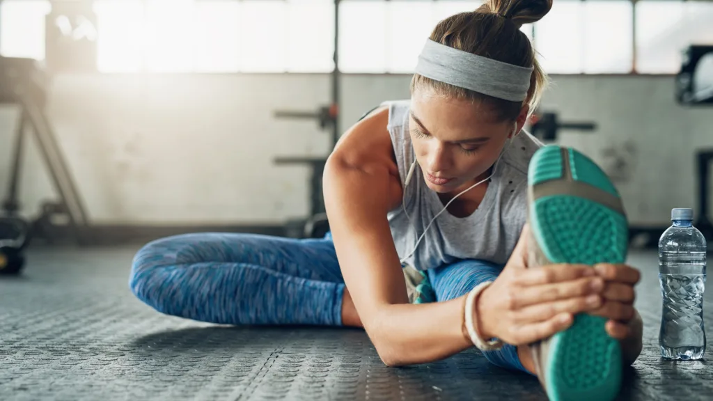 Woman stretching her hamstrings on the gym floor. She has on a grey headband, wire earphones, blue pants and blue soles of her shoes. There is a water bottle beside her, she seems focused and is looking down. New pet-friendly apartment homes for rent with private fenced backyards in Arizona, Texas, Florida, and North Carolina with pool, pickleball, dog park, gym, clubhouse and gated community. *No breed or weight restrictions. Yardly