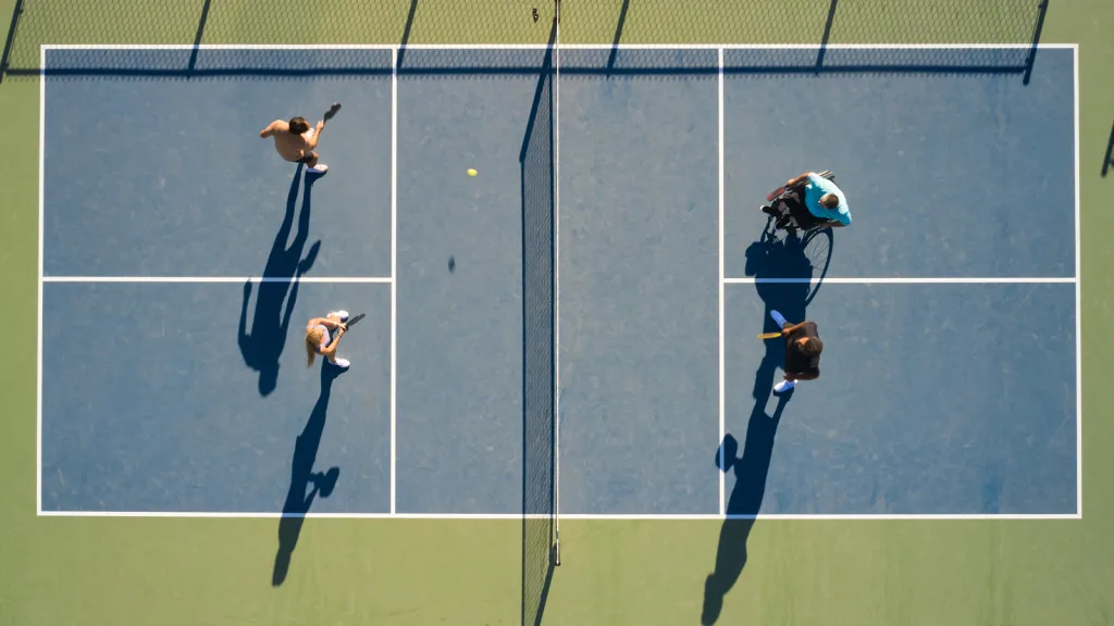 Aerial photo of pickleball game, there are 4 players 3 of them are standing one is playing from his wheelchair. There are 3 men and one woman playing, the ball is midair headed toward one team after it was served by the other. New pet-friendly apartment homes for rent with private fenced backyards in Arizona, Texas, Florida, and North Carolina with pool, pickleball, dog park, gym, clubhouse and gated community. *No breed or weight restrictions. Yardly