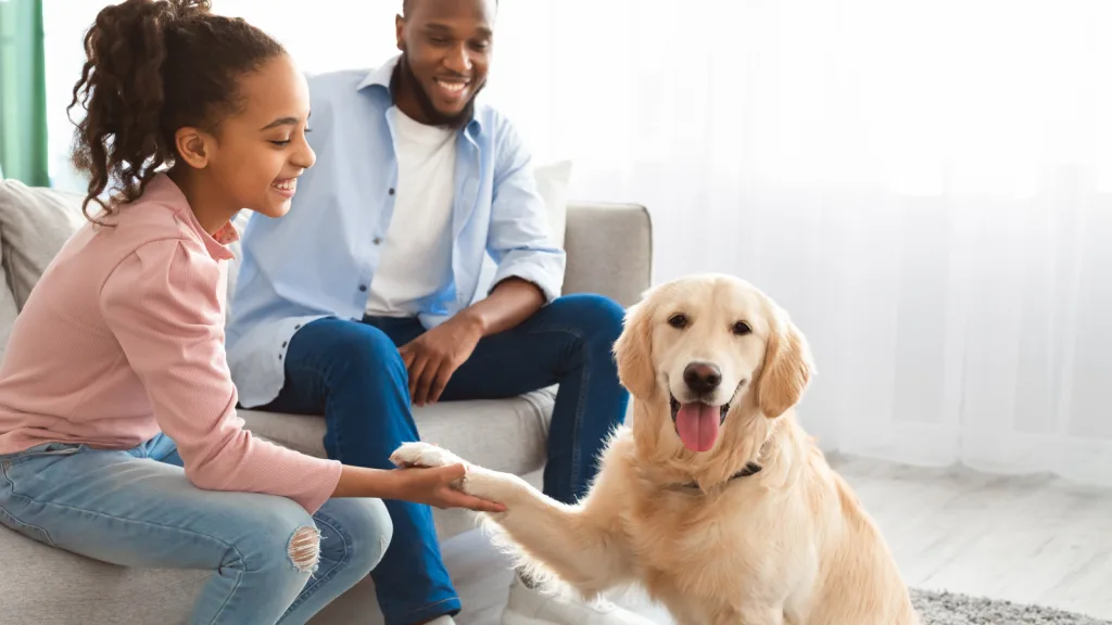 Man, and daughter admiring their pet Golden Retriever in their new living room. The pre-teen girl is holding the dog's paw and leaning in. The dog looks happy and relaxed at the camera. The dad is observing the two and smiling. New pet-friendly apartment homes for rent with private fenced backyards in Arizona, Texas, Florida, and North Carolina with pool, pickleball, dog park, gym, clubhouse and gated community. *No breed or weight restrictions. Yardly